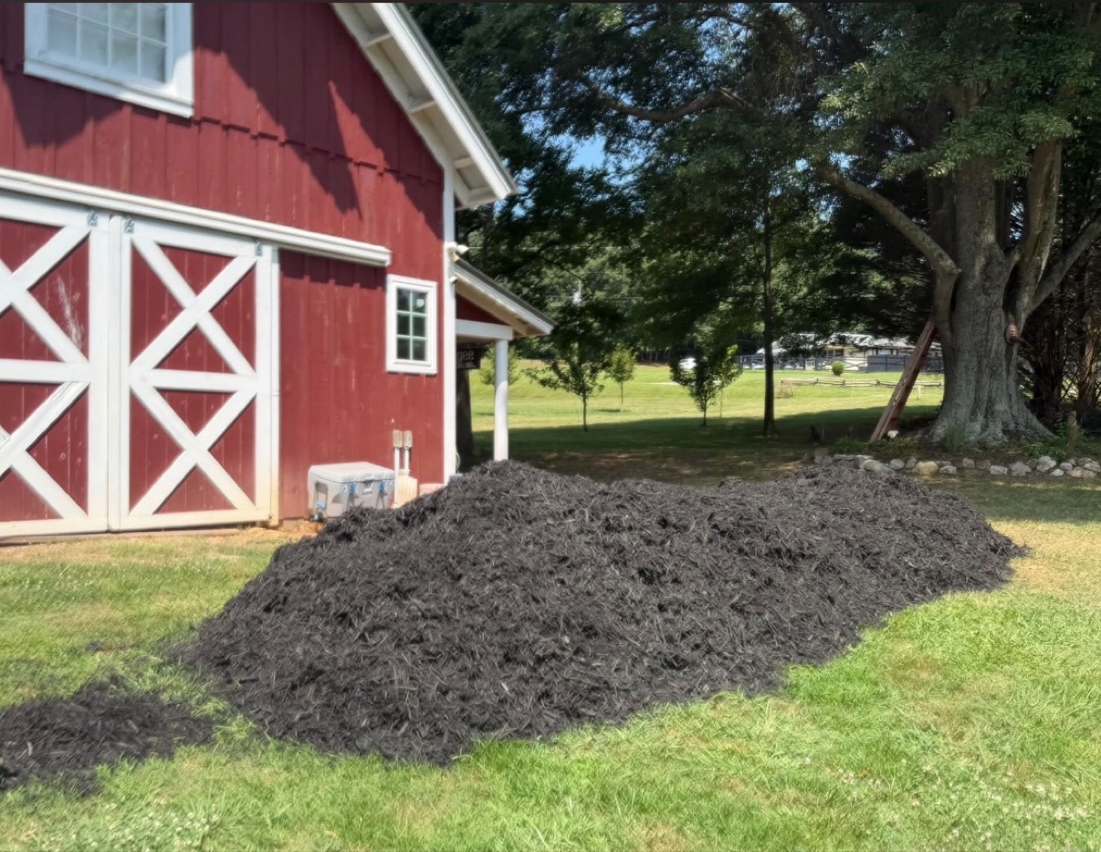 Black mulch pile delivered beside a red barn